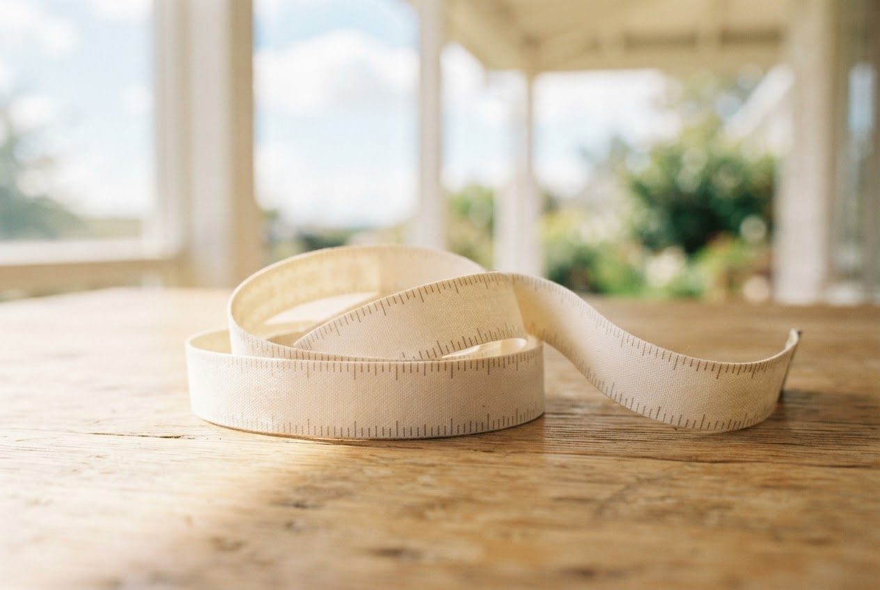 A soft flexible fabric sewing tape measure with clear printed inch numbers, loosely curled on a sunlit wooden table