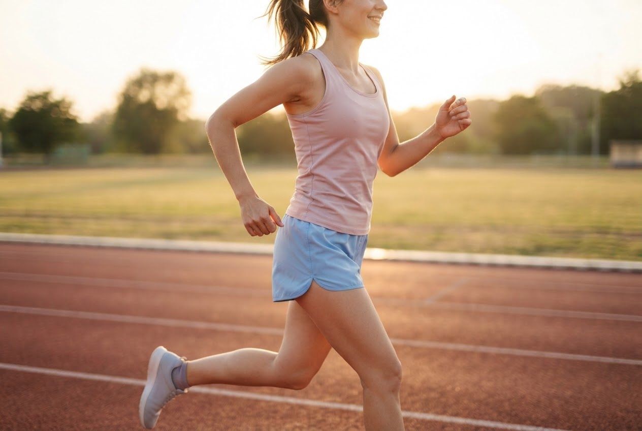 Close view of a runner's torso and arms mid-stride with nothing carried and nothing worn, clean uncluttered silhouette against an empty track