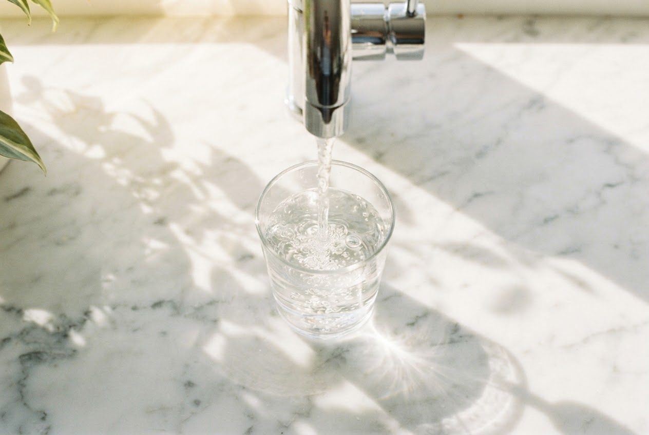 A glass of water being filled at a kitchen tap with sunlight through the window